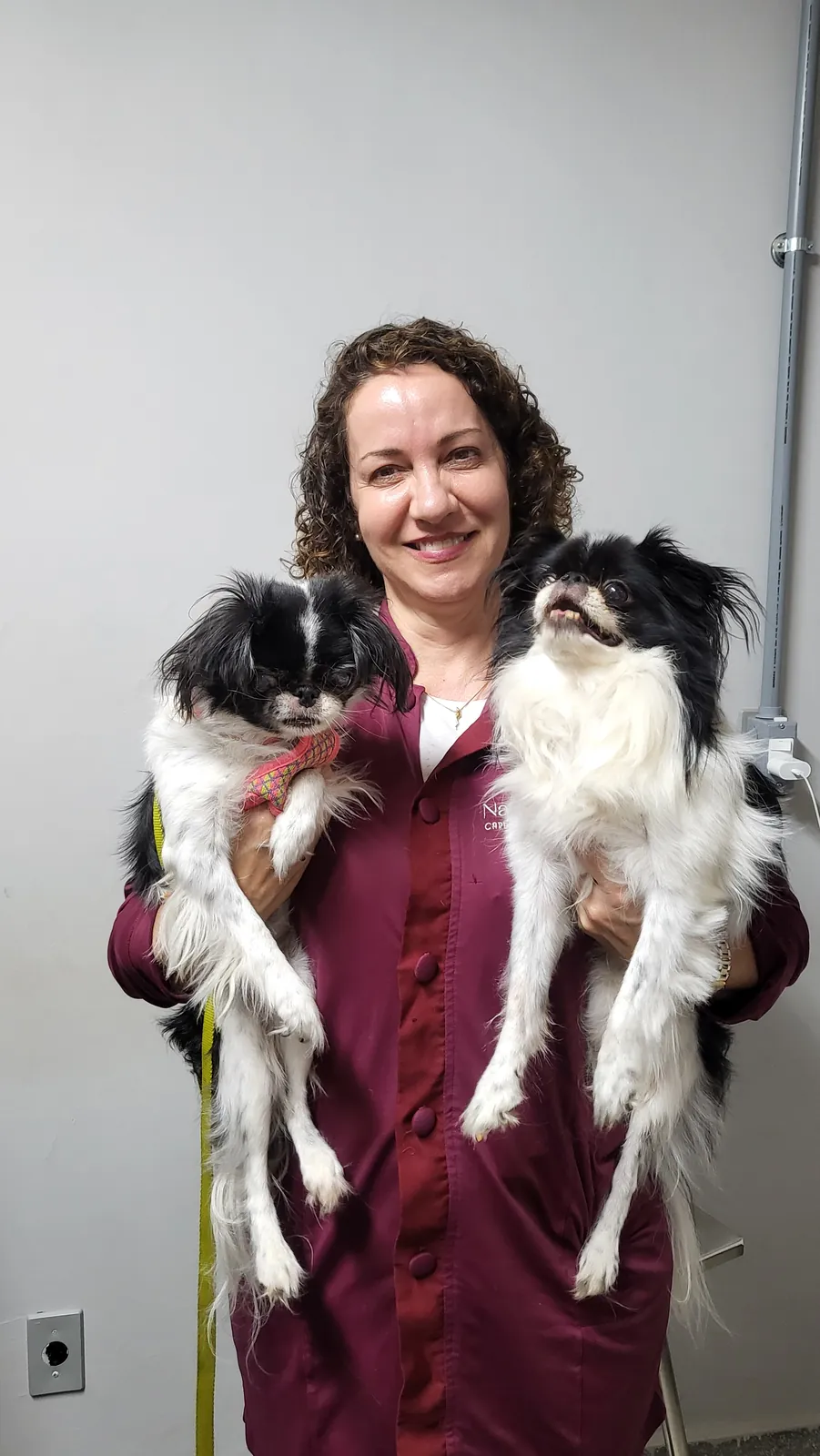 Dra. Nanci Diniz, de uniforme vinho, segurando dois cães no colo